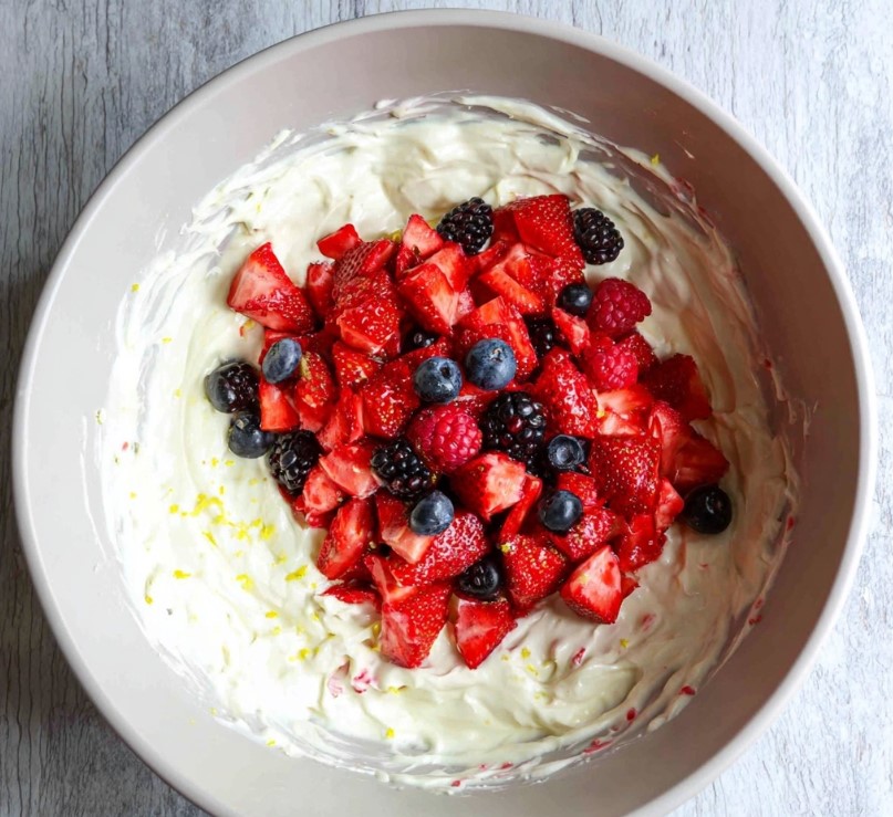 Chopped fruits added on top of a creamy mixture in a bowl before stirring and final mixing.