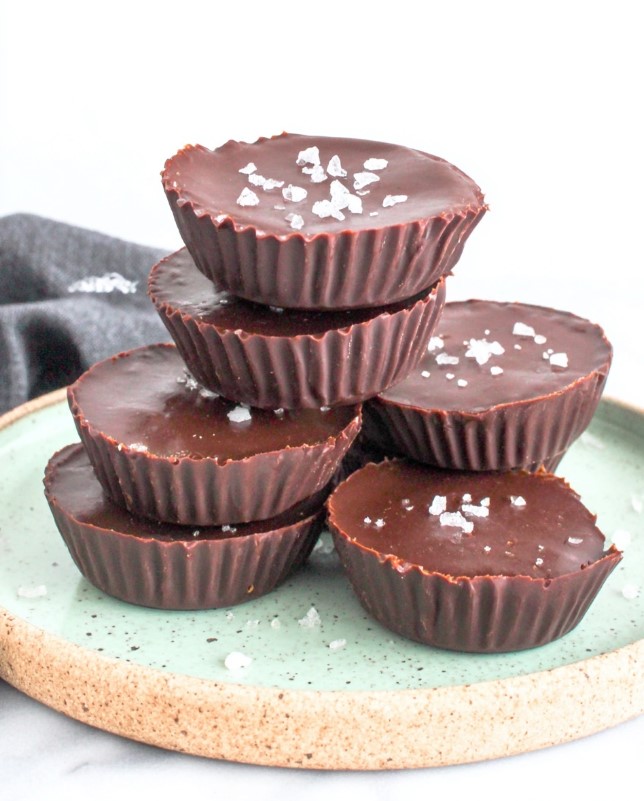 Keto Chocolate Peanut Butter Cups - High stack of chocolate bites on green plate with empty muffin tin in background, clean white setting
