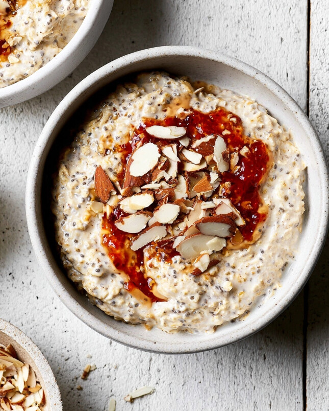 Top-down view of a creamy overnight oat bowl garnished with a layer of jam/berry sauce and topped with almond slices