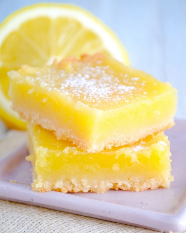 Finished lemon bars after baking and cooling, with a lemon custard layer over a biscuit base and a dusting of powdered sugar.