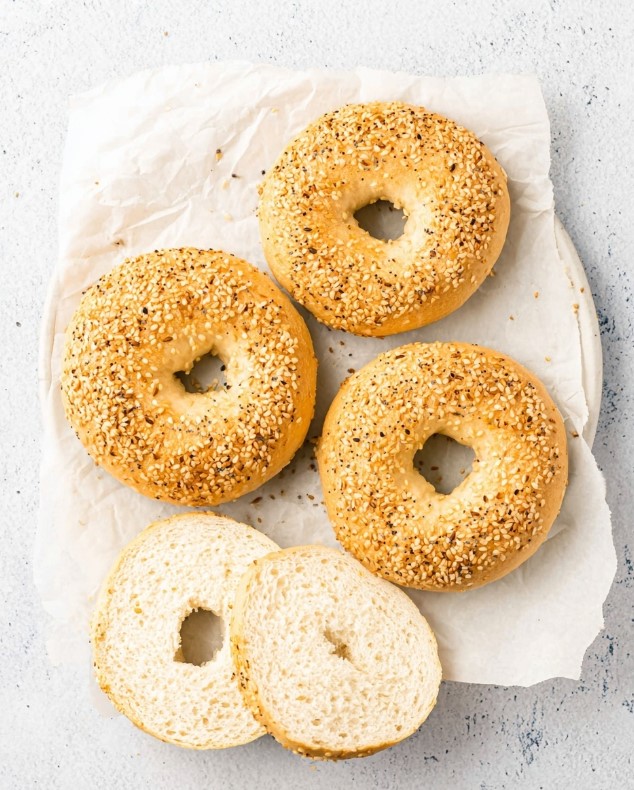 The bagel after baking covered with sesame seeds, displaying a cut slice that reveals its fluffy, ready-to-eat internal texture.