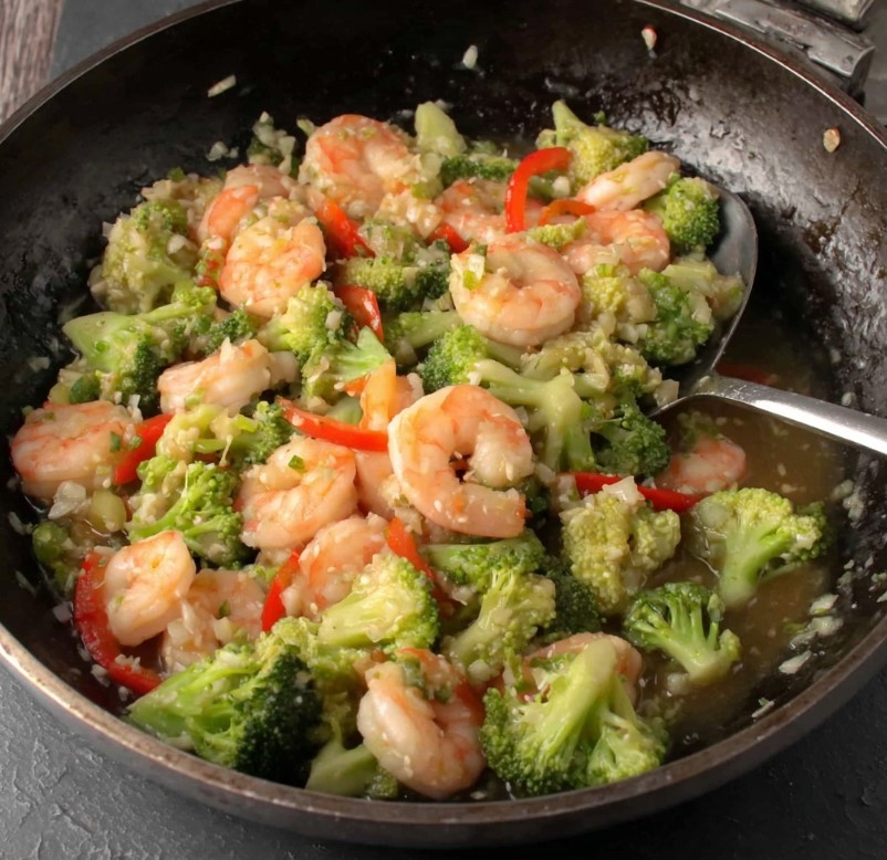 Shrimp being sautéed with broccoli and red peppers in a skillet as the sauce thickens.