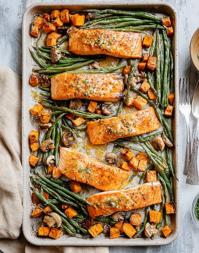 A complete sheet pan dinner featuring roasted salmon fillets glazed in tahini, surrounded by golden sweet potato cubes, roasted mushrooms, and vibrant green beans, ready to serve.