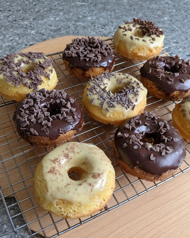 Freshly baked donuts cooling on a wire rack, drizzled with glossy dark and white chocolate glazes
