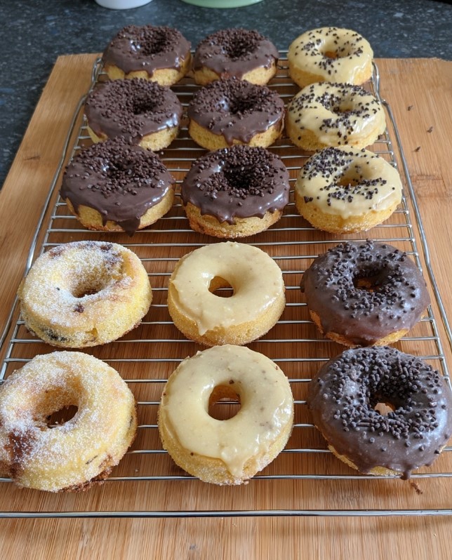 A wire rack filled with an assortment of decorated donuts—chocolate, vanilla, and sugar-coated—setting before serving