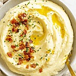 Close-up of creamy cauliflower puree topped with melted butter, crispy bacon bits, and fresh chives, ready to serve.
