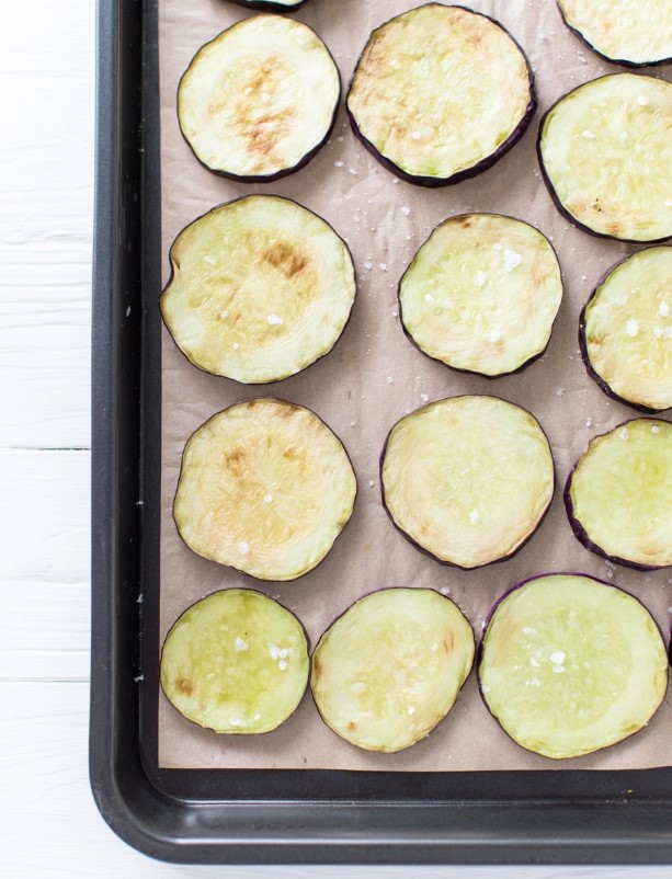 Slices of raw eggplant arranged neatly on a baking sheet, ready to be roasted in the oven.