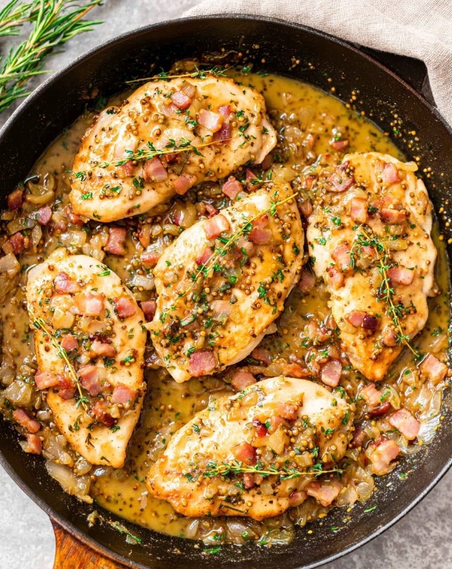 The stage of cooking chicken breasts in the pan after browning them, then leaving them to boil and hold together inside the mustard sauce with onions, bacon and herbs.