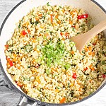 Better-Than-Takeout Keto Cauliflower Fried Rice for Busy Weeknights A close-up, top-down view of a plate of golden fried cauliflower rice mixed with bright red peppers and yellow egg bits, freshly garnished with chopped green scallions.