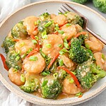 Plated shrimp and broccoli coated in glossy sauce, garnished with green onions, ready to serve.