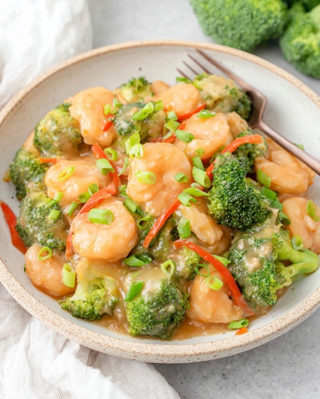 Plated shrimp and broccoli coated in glossy sauce, garnished with green onions, ready to serve.