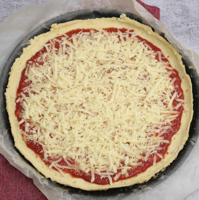 Keto Almond Flour Pizza Crust - raw dough topped with red tomato sauce and shredded mozzarella ready for the oven