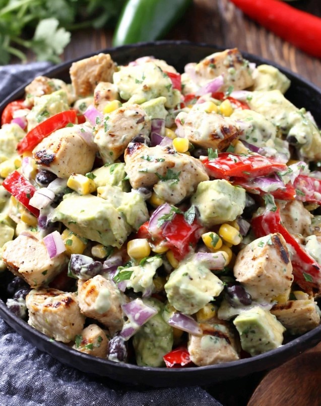 A vibrant chicken avocado salad mixed thoroughly with black beans and corn, fully coated in a creamy green dressing, ready to eat