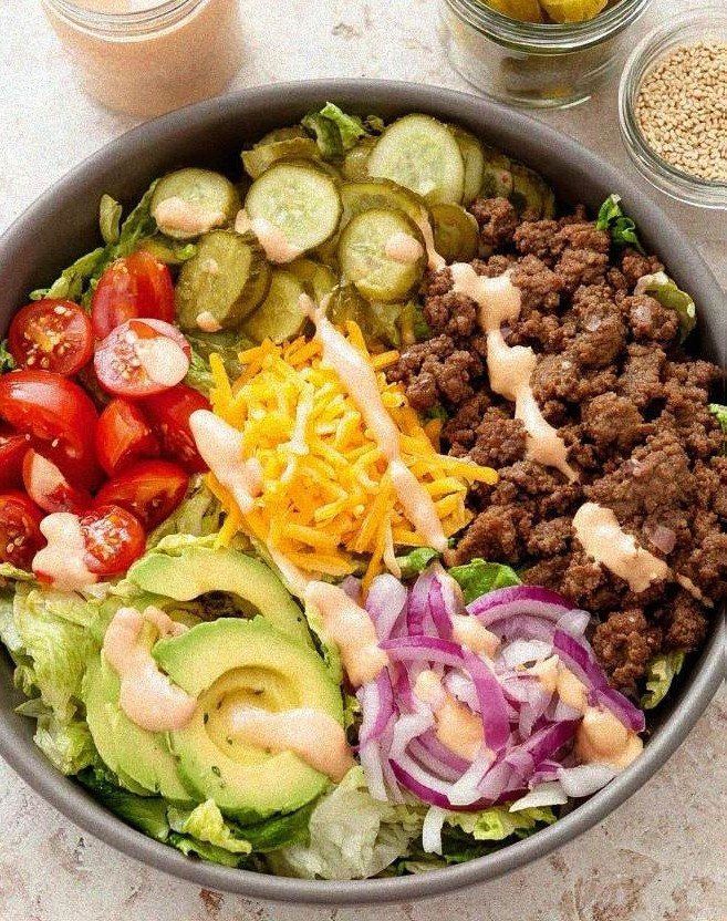 Wide bowl filled with crisp iceberg lettuce, caramelized ground beef crumbles, sharp cheddar, cherry tomatoes, and pink sauce