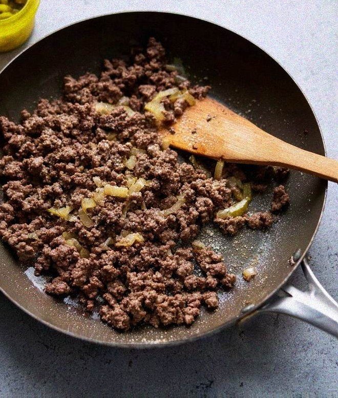 Ground beef and onions browning in a wide skillet, broken apart with a wooden spoon
