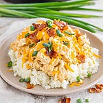 Plated slow cooker keto crack chicken served over a bed of cauliflower rice and topped with melted cheddar cheese, chopped bacon, and green onions