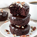 A stack of fudgy low carb Texas sheet cake bites on a white plate covered in shiny chocolate glaze and toasted pecans