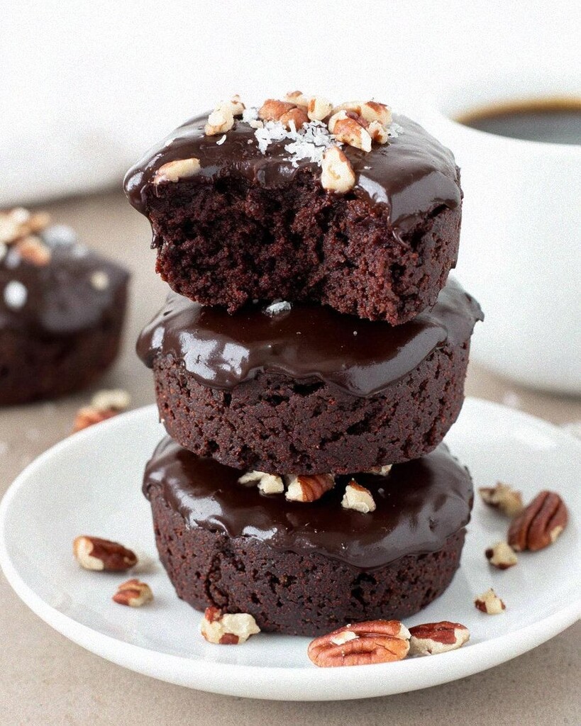 A stack of fudgy low carb Texas sheet cake bites on a white plate covered in shiny chocolate glaze and toasted pecans