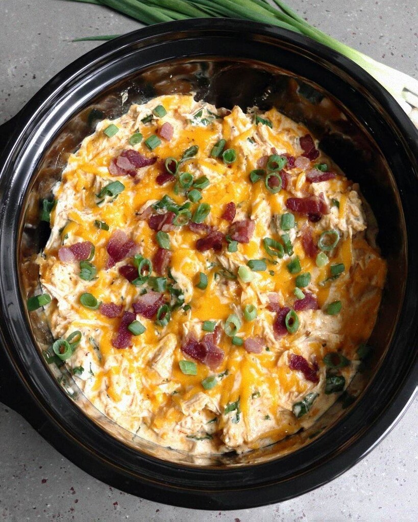Slow cooker keto crack chicken inside the crockpot with a thick creamy sauce, covered in melted cheddar cheese, bacon pieces, and sliced green onions