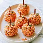 Bright orange pumpkin shaped rice krispie treats decorated with pretzel stems and green pumpkin seeds on a light plate