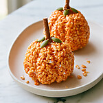 Two finished orange pumpkin treats showing their crispy texture and pretzel stems on an oval plate