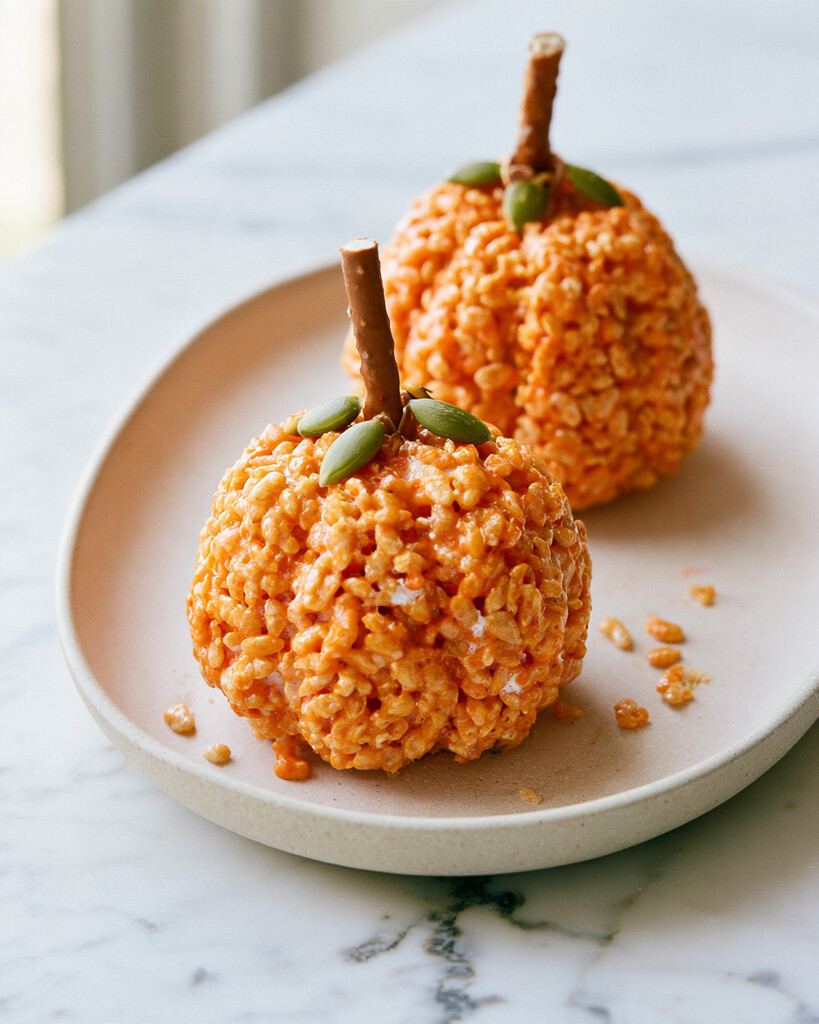 Two finished orange pumpkin treats showing their crispy texture and pretzel stems on an oval plate