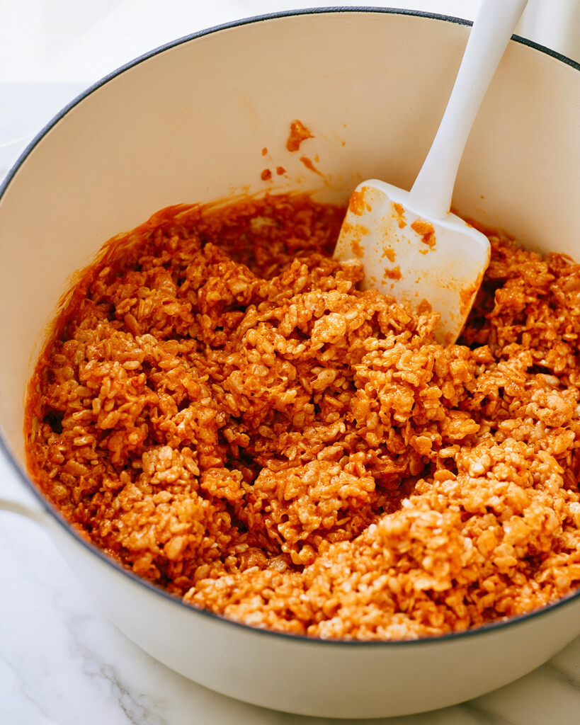 Folding crispy rice cereal into an orange marshmallow mixture with a silicone spatula
