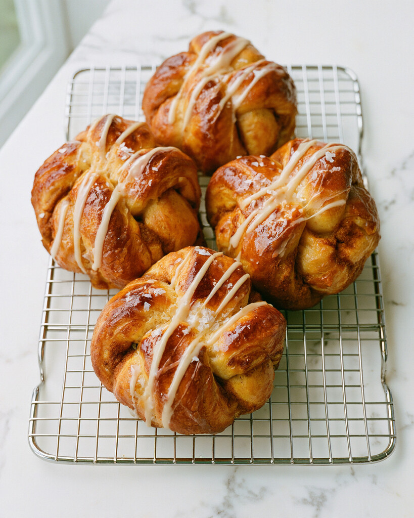Golden baked salted maple pumpkin spice cruffins on a wire cooling rack with white cream cheese drizzle and flaky sea salt