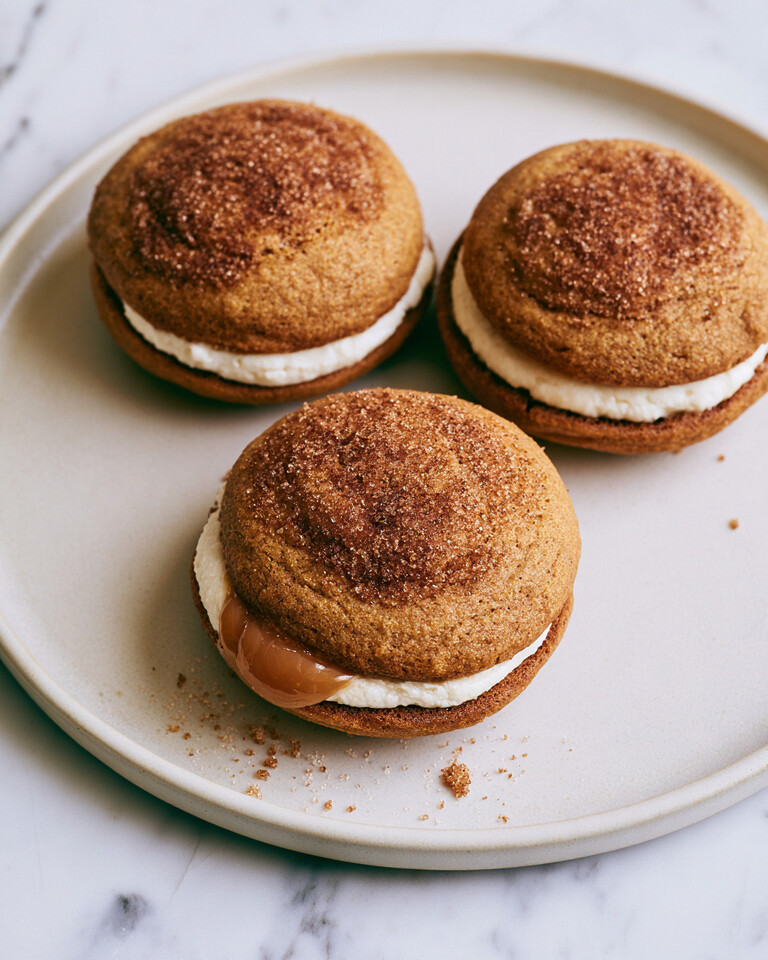 Assembled apple cider whoopie pies on a light plate showing golden cinnamon-sugar tops and cream cheese caramel filling