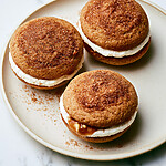 Apple cider whoopie pies arranged on a ceramic plate with golden crusted edges and creamy caramel centers