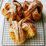 Freshly baked golden pumpkin cruffins on a metal cooling rack with white maple cream cheese glaze flowing over the layers