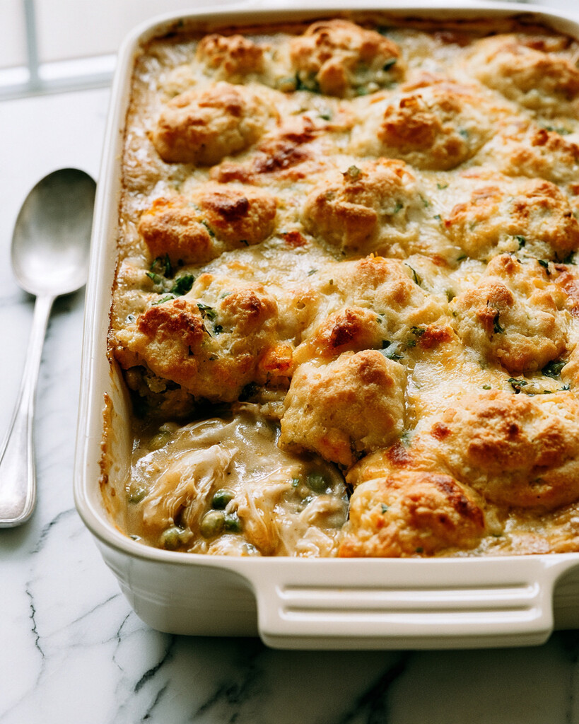 Cheddar Biscuit Chicken Cobbler in a ceramic baking dish with one portion scooped out showing creamy chicken filling