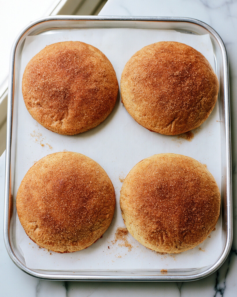 Baked golden apple cider whoopie pie cakes topped with sparkling cinnamon sugar cooling on a parchment-lined sheet