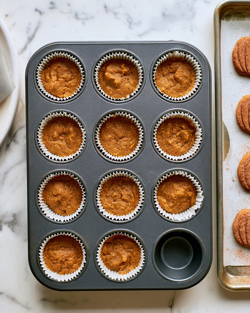Baked golden sugar cookie crusts sitting inside white paper liners in a metal muffin tin