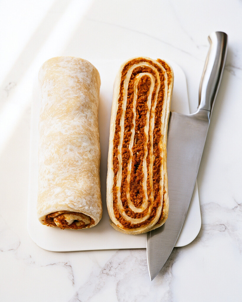 Rolled crescent dough log beside a lengthwise-sliced half showing layers of spiced pumpkin filling on a white board