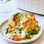 A portion of Cheddar Biscuit Chicken Cobbler served on a white plate with golden crust and vegetable gravy