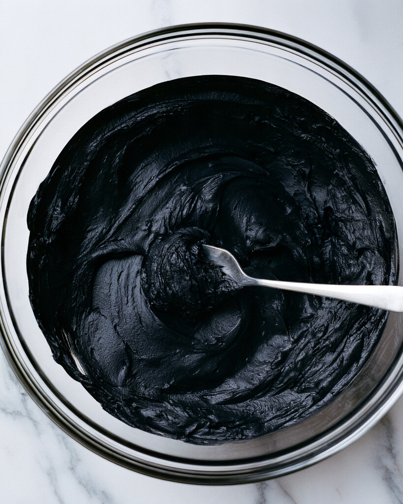 Thick, smooth black cocoa buttercream scooped with a spoon in a glass bowl