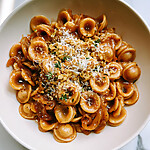 Serving dish of French onion pasta topped with shredded Gruyère cheese, toasted garlic breadcrumbs, and fresh green herb leaves